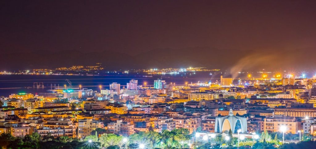 Una nuova Piazza: Pratzita – Piazzetta Società Rari Nantes. La foto ritrae uno scorcio panoramico della città di Cagliari di notte, tutta illuminata.
