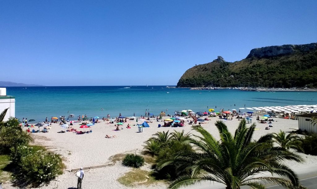 Tempo di mare e le spiagge di Cagliari e dintorni. La Spiaggia Del Poetto. In questa foto vediamo un panorama della spiaggia con alcuni bagnanti e sullo sfondo la Sella del Diavolo