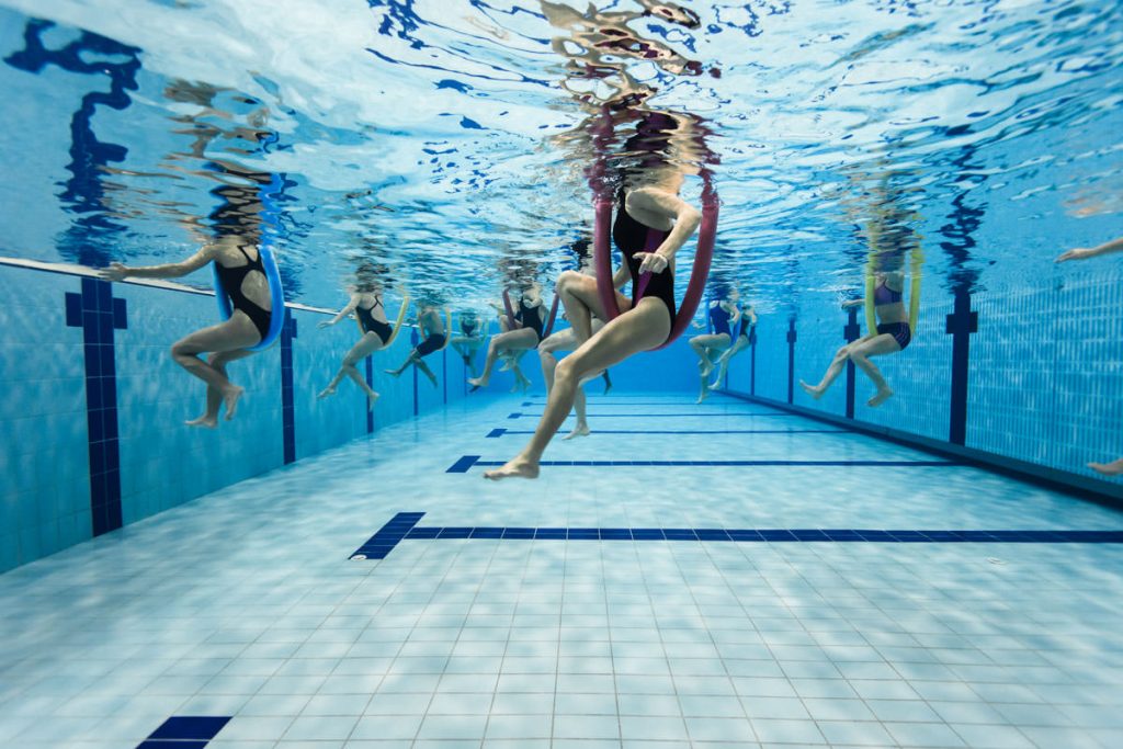 Lo Sport alla cagliaritana: Il Nuoto. Dove praticarlo? La foto vede il fondale della piscina Acquasport in cui alcune utenti fanno esercizi di ginnastica in acqua con degli attrezzi