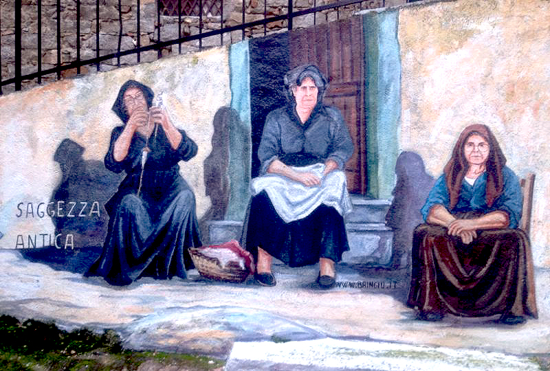 Murales che raffigura 3 donne anziane delle Blue Zones sedute davanti alla porta di ingresso. una è intenta a filare. sulla sinistra la frase saggezza antica
