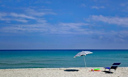 Spiaggia deserta con ombrellone sdraio e sullo sfondo mare e cielo azzurro