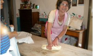 Albertina Piras la donna in primo piano impasta su un taovlo di legno e prepara i dolci di saba