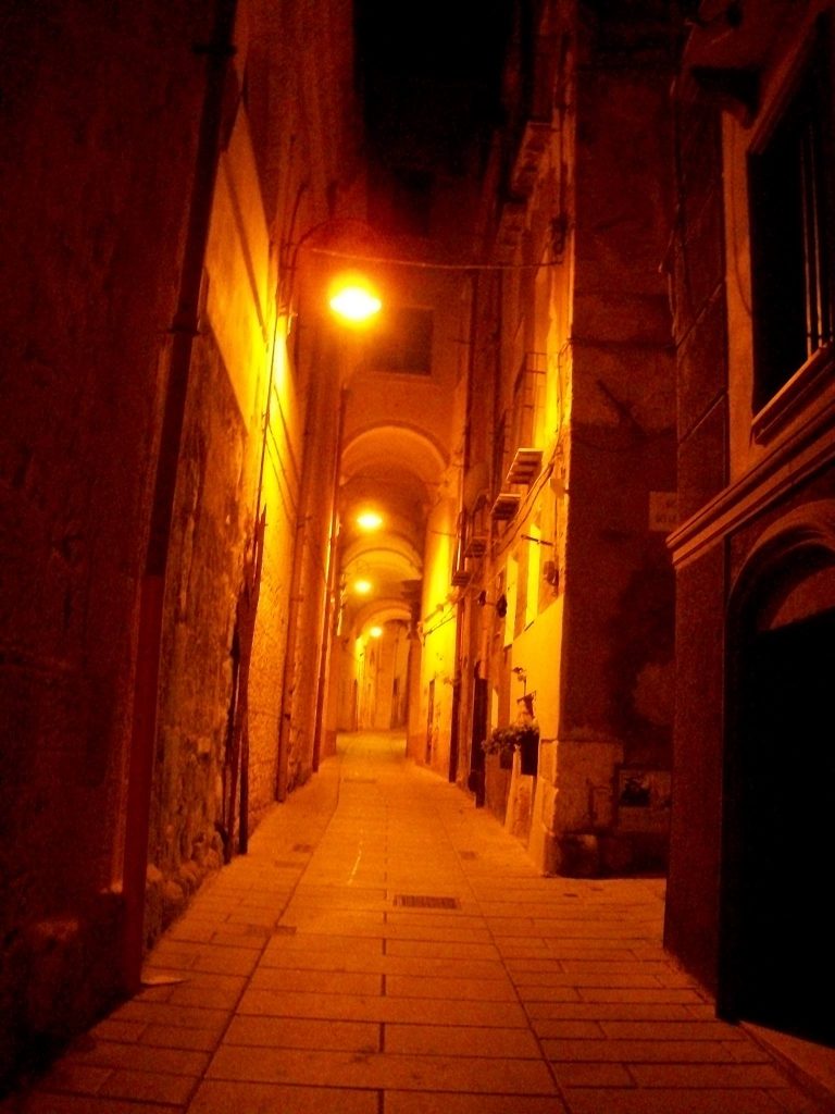una via cittadina durante la notte appena illuminata dai lampioni Cagliari Dei Misteri