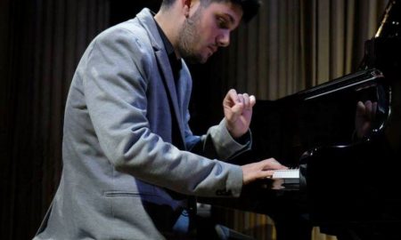 Alessio Zucca, uomo seduto in abito grigio che suona davanti al piano