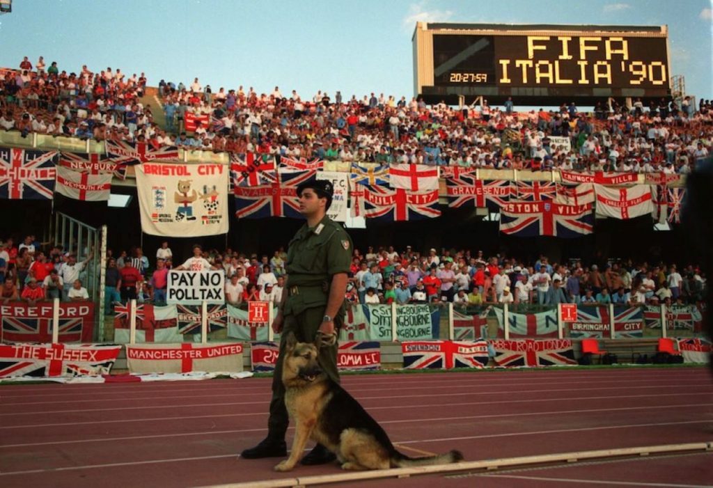 un agente in primo piano con un cane e sullo sfondo gli spalti dello stadio Sant'Elia
