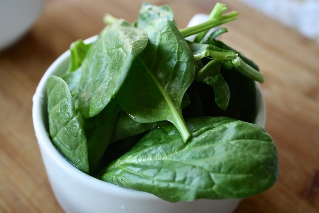 ciotola di ceramica bianca con foglie di spinaci crudi.