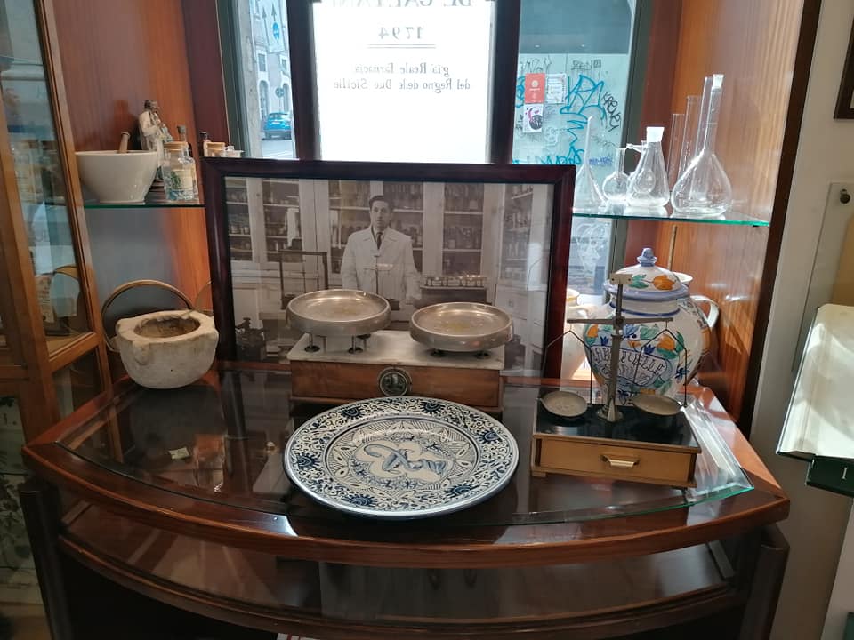 Uno dei banconi della farmacia storica De Gaetani in cui sono esposte le bilance, i piatti, i vasi di Caltagirone, il mortaio di marmo ricavato dalla testa mozzata di una delle statue dei Borbone, la foto del Prof. De Gaetani, padre dell'ultima discendente della farmacia
