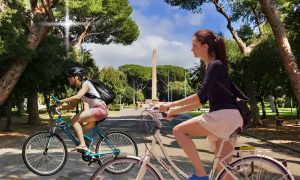 Biciclette e monopattini - ragazze in bici lungo il viale