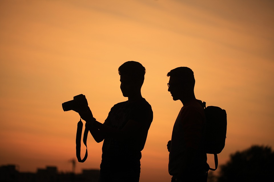 sfondo arancione con due uomini intenti a guardare una macchina fotografica