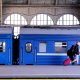 Train Bleu - viaggiatore con trolley rosso accanto ad un treno blu