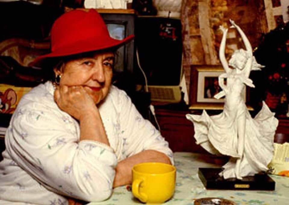 Alda Merini seduta al tavolo con un cappello rosso e un tazzone del caffè giallo