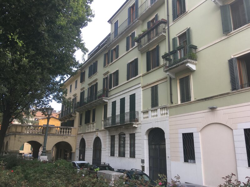 Riva San Lorenzo .Facciata laterale verde e bianca con inferriate e balconi dove sono attaccati dei vasi di fiori