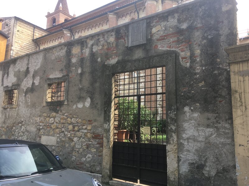 Riva San Lorenzo. Il muro esterno dell'ingresso posteriore in pietra e mattoni, un cancello e delle inferriate